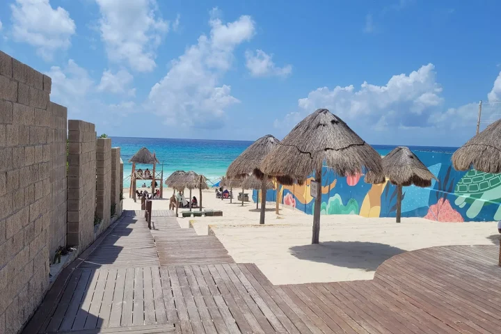 The entrance to Play Marlin in Cancun, shosing tiki umbrellas and sand with the caribbean in the distance