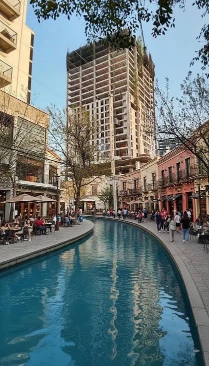 A view of the man-made waterway and riverwalk path of Santa Lucia in Monterrey, Mexico, with outdoor restaurant tables